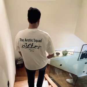Chico joven moreno de espaldas bajando las escaleras con una camiseta blanca que tiene un dibujo de unos pingüinos con la frase The Arctic Squad