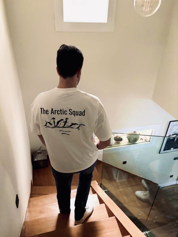 Chico joven moreno de espaldas bajando las escaleras con una camiseta blanca que tiene un dibujo de unos pingüinos con la frase The Arctic Squad
